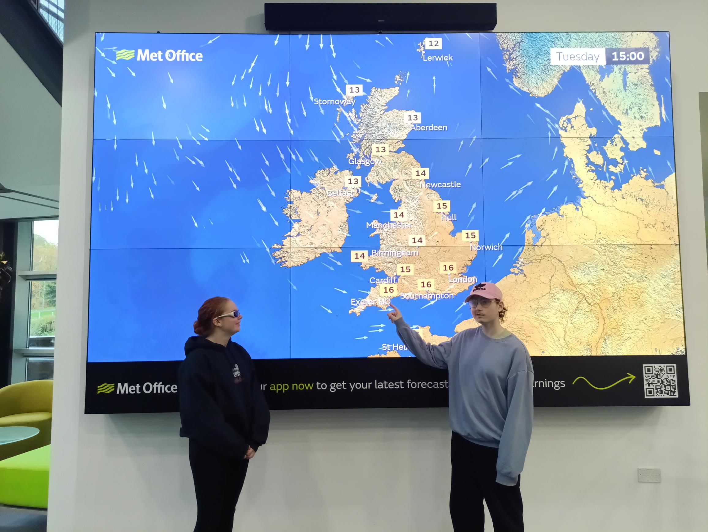 Students standing in front of a large screen with a weather map of the UK on.